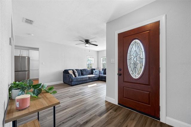 foyer entrance with a ceiling fan, visible vents, baseboards, and wood finished floors