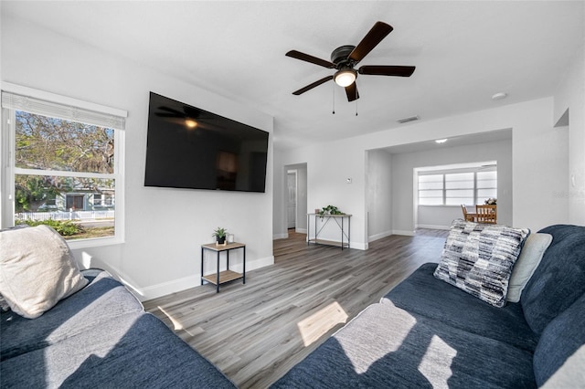 living area with a ceiling fan, visible vents, baseboards, and wood finished floors