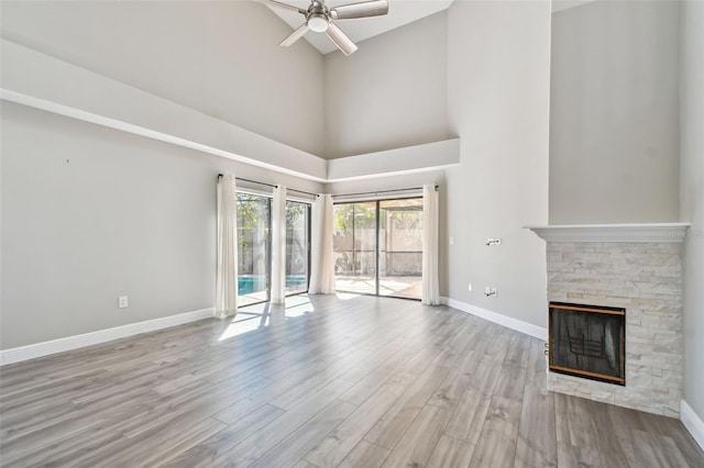 unfurnished living room with a stone fireplace, light hardwood / wood-style flooring, ceiling fan, and a towering ceiling