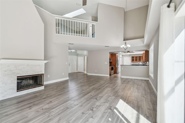 unfurnished living room featuring a fireplace, sink, a high ceiling, light hardwood / wood-style floors, and an inviting chandelier