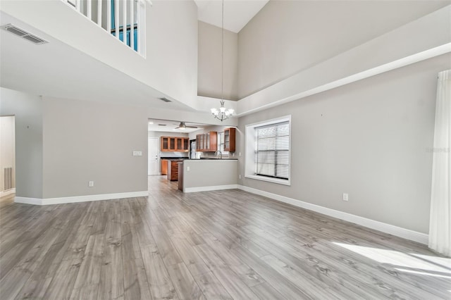 unfurnished living room with ceiling fan with notable chandelier, a towering ceiling, and light wood-type flooring