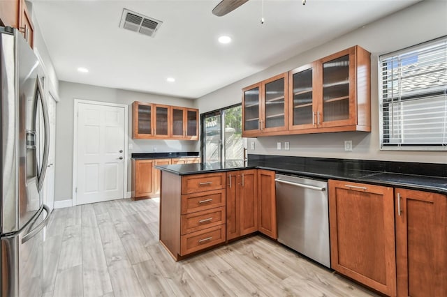 kitchen with dark stone countertops, ceiling fan, kitchen peninsula, stainless steel appliances, and light hardwood / wood-style flooring