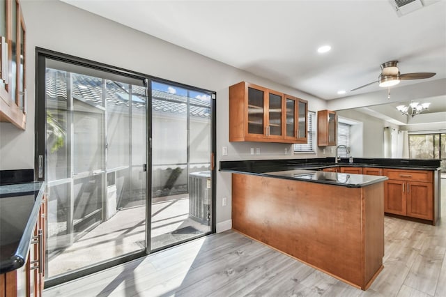 kitchen with ceiling fan with notable chandelier, kitchen peninsula, sink, and light hardwood / wood-style flooring