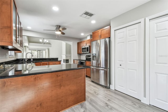 kitchen featuring sink, light wood-type flooring, kitchen peninsula, stainless steel appliances, and ceiling fan with notable chandelier