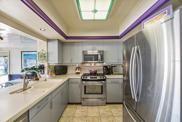 kitchen with sink, light tile patterned floors, appliances with stainless steel finishes, gray cabinetry, and a raised ceiling