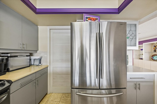 kitchen with gray cabinetry, light tile patterned floors, stainless steel fridge, and range