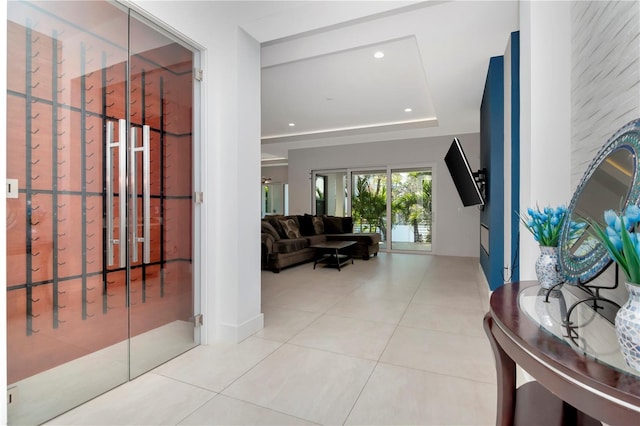 hall with light tile patterned floors and a tray ceiling