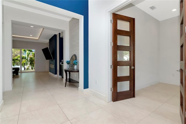 corridor featuring a tray ceiling and light tile patterned flooring