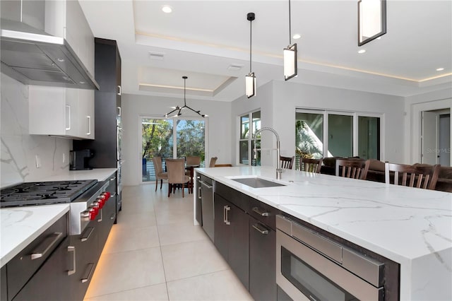 kitchen with backsplash, a raised ceiling, appliances with stainless steel finishes, wall chimney exhaust hood, and pendant lighting