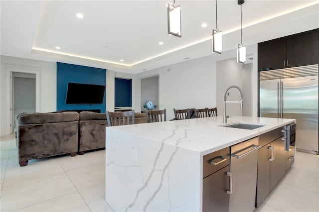 kitchen featuring a center island with sink, stainless steel built in fridge, sink, and decorative light fixtures