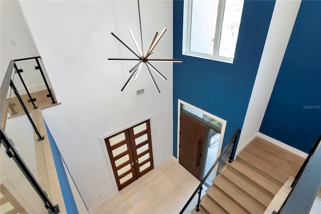 staircase featuring an inviting chandelier, french doors, and a high ceiling