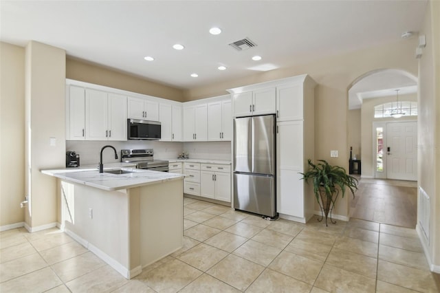 kitchen with appliances with stainless steel finishes, kitchen peninsula, light tile patterned floors, and white cabinets