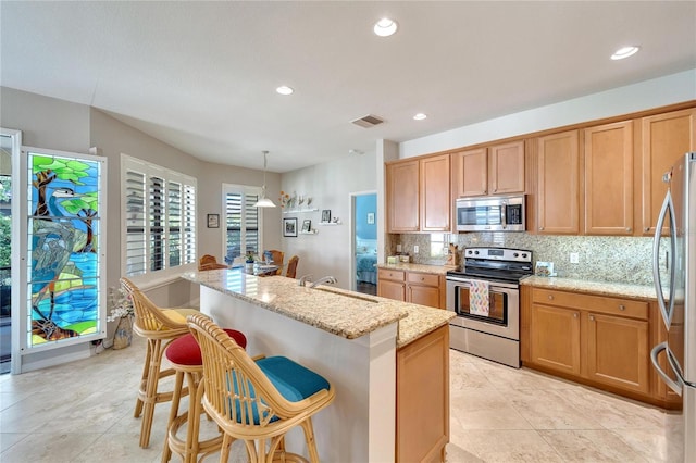 kitchen featuring appliances with stainless steel finishes, sink, hanging light fixtures, a kitchen island with sink, and light stone countertops