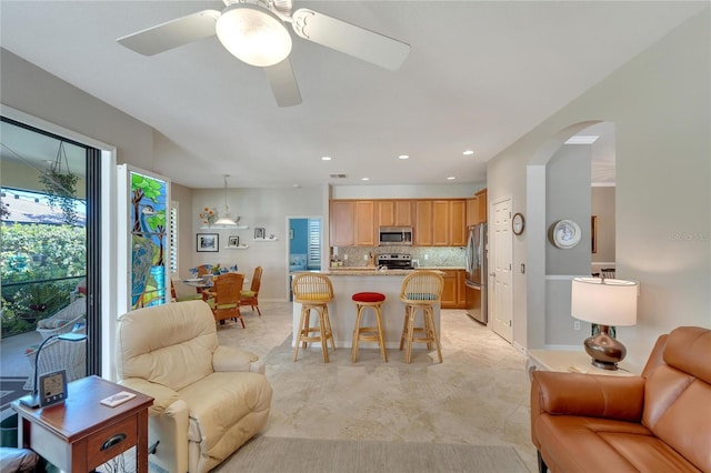 kitchen featuring decorative light fixtures, backsplash, a kitchen bar, ceiling fan, and stainless steel appliances