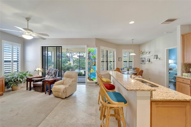 kitchen featuring sink, decorative light fixtures, light brown cabinets, a kitchen breakfast bar, and light stone countertops