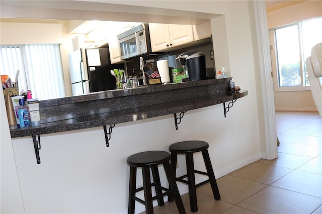 kitchen with light tile patterned floors, a breakfast bar, backsplash, stainless steel appliances, and white cabinets