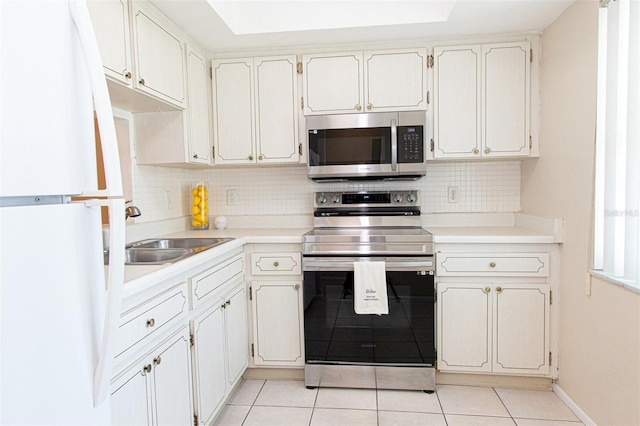 kitchen featuring sink, light tile patterned floors, appliances with stainless steel finishes, backsplash, and white cabinets