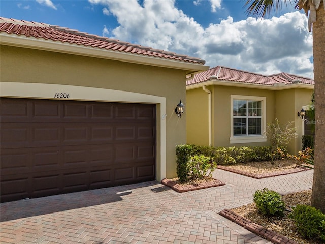 exterior space with an attached garage, a tiled roof, decorative driveway, and stucco siding