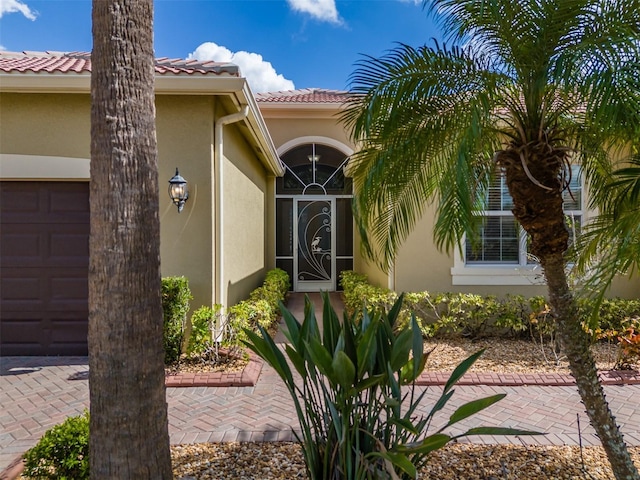 view of exterior entry with a tile roof, an attached garage, and stucco siding