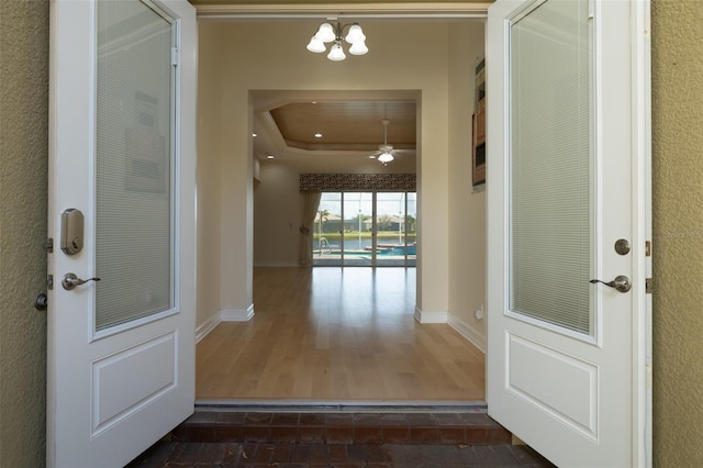 entryway with a tray ceiling, dark wood-style flooring, baseboards, and an inviting chandelier