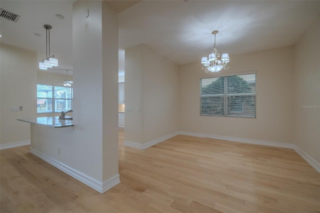 unfurnished dining area featuring light wood finished floors, visible vents, a sink, a chandelier, and baseboards