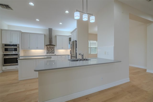 kitchen featuring stainless steel appliances, visible vents, a sink, a peninsula, and wall chimney exhaust hood