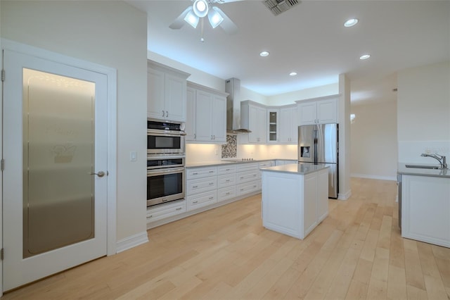 kitchen featuring stainless steel appliances, a kitchen island, visible vents, light wood-type flooring, and wall chimney exhaust hood