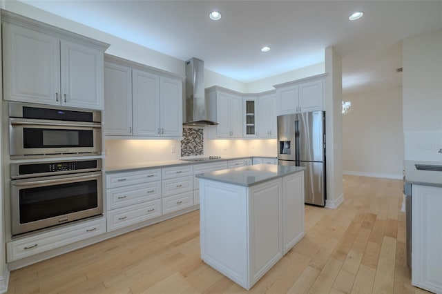 kitchen featuring a center island, light countertops, light wood-style flooring, appliances with stainless steel finishes, and wall chimney exhaust hood