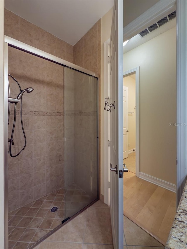 full bathroom featuring tiled shower, visible vents, baseboards, and wood finished floors