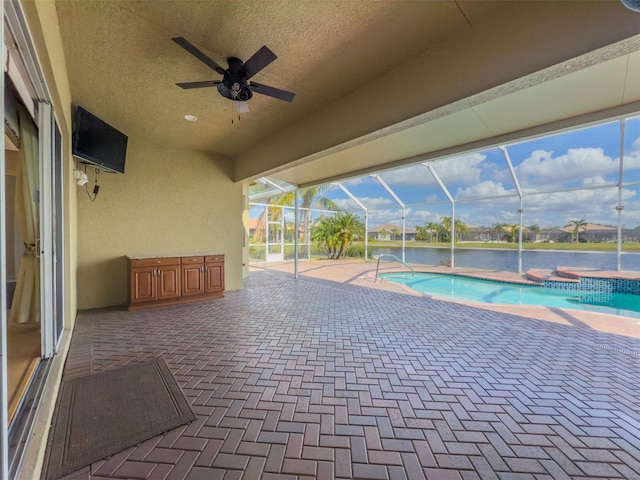 outdoor pool with a water view, glass enclosure, a patio area, ceiling fan, and a jacuzzi