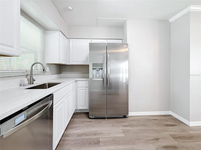 kitchen with sink, white cabinetry, light stone counters, appliances with stainless steel finishes, and light hardwood / wood-style floors