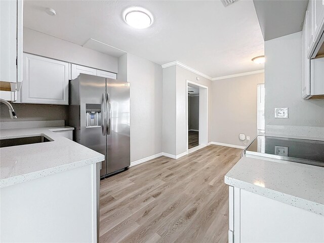 kitchen with white cabinetry, stainless steel fridge, sink, and light stone counters