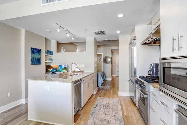 kitchen featuring sink, white cabinetry, light stone counters, premium appliances, and wall chimney range hood