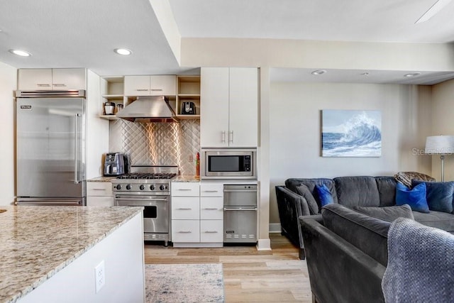 kitchen featuring tasteful backsplash, white cabinets, built in appliances, light stone counters, and light wood-type flooring