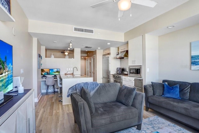 living room featuring ceiling fan, sink, and light wood-type flooring