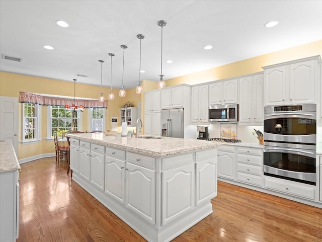 kitchen featuring white cabinetry, appliances with stainless steel finishes, hanging light fixtures, and a center island with sink