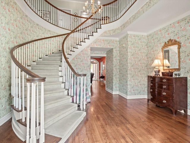 staircase featuring hardwood / wood-style flooring, a towering ceiling, ornamental molding, and an inviting chandelier