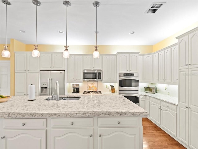 kitchen with hanging light fixtures, white cabinetry, appliances with stainless steel finishes, and a kitchen island with sink