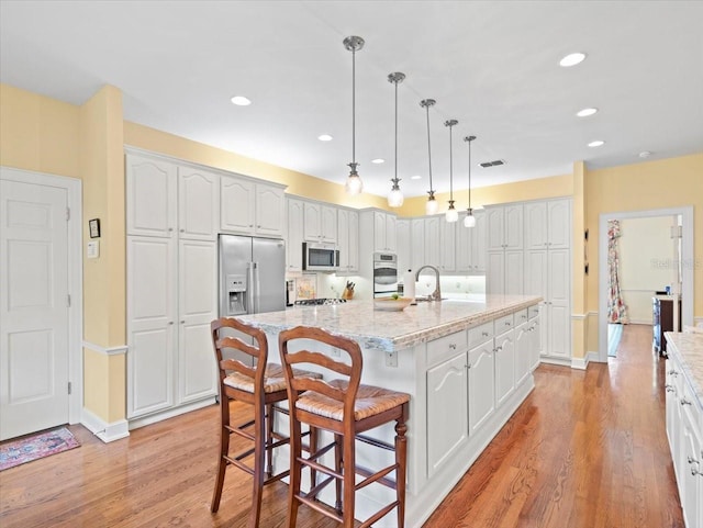 kitchen featuring white cabinetry, appliances with stainless steel finishes, pendant lighting, light stone countertops, and a kitchen island with sink