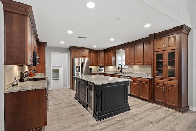 kitchen featuring light hardwood / wood-style flooring, a kitchen island, stainless steel appliances, light stone countertops, and decorative backsplash