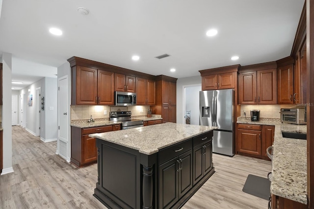 kitchen featuring light stone countertops, light wood-type flooring, stainless steel appliances, and a kitchen island