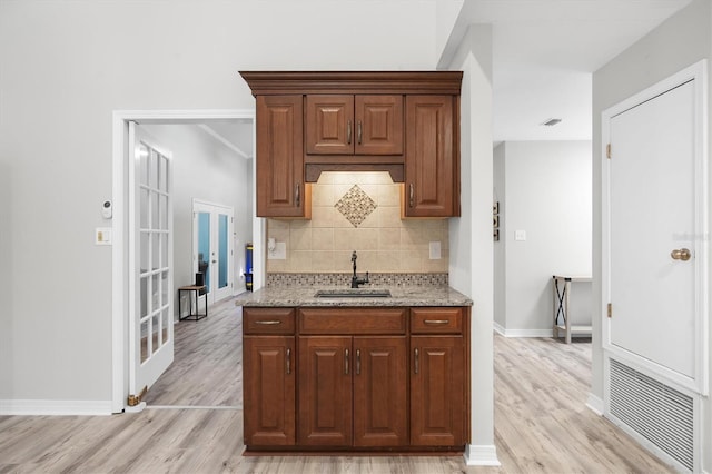 kitchen with light stone counters, backsplash, sink, and light wood-type flooring