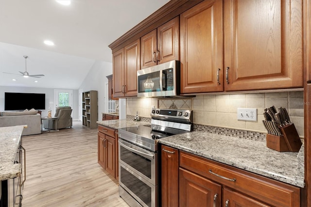 kitchen featuring light hardwood / wood-style flooring, ceiling fan, appliances with stainless steel finishes, light stone counters, and vaulted ceiling