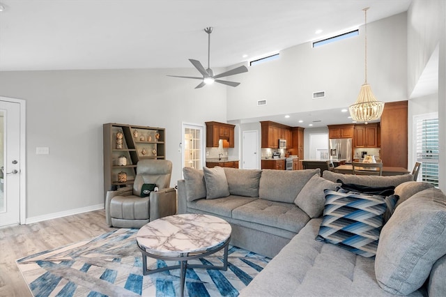 living room with ceiling fan with notable chandelier, a high ceiling, and light wood-type flooring