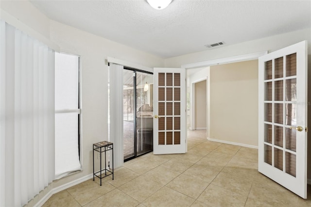 unfurnished room with french doors, a textured ceiling, and light tile patterned floors