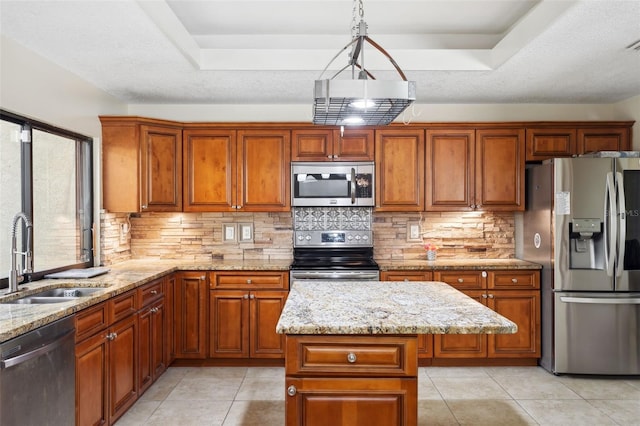 kitchen featuring stainless steel appliances, a tray ceiling, sink, and a kitchen island