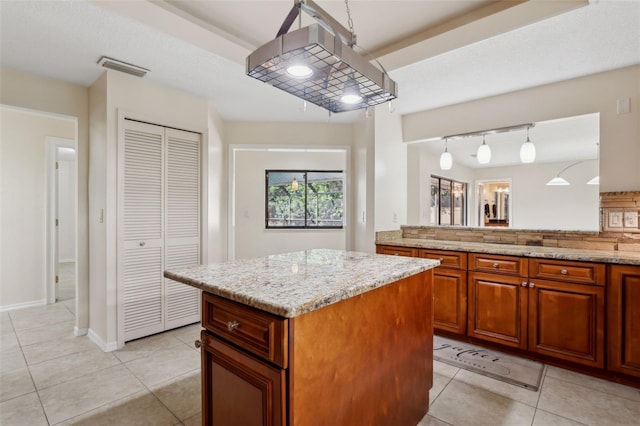 kitchen with light tile patterned flooring, a kitchen island, rail lighting, hanging light fixtures, and light stone counters