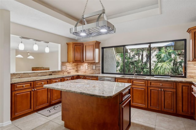 kitchen with sink, hanging light fixtures, a tray ceiling, a kitchen island, and decorative backsplash