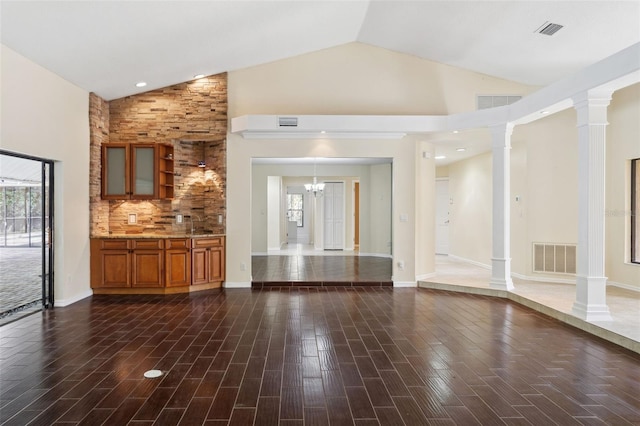 unfurnished living room featuring dark hardwood / wood-style flooring, a notable chandelier, high vaulted ceiling, and ornate columns