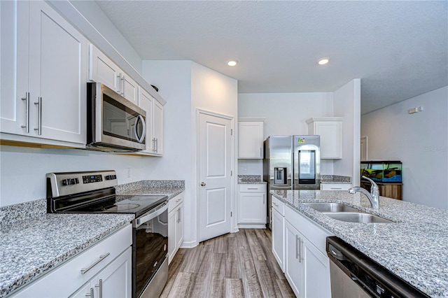 kitchen featuring sink, light stone counters, stainless steel appliances, light hardwood / wood-style floors, and white cabinets